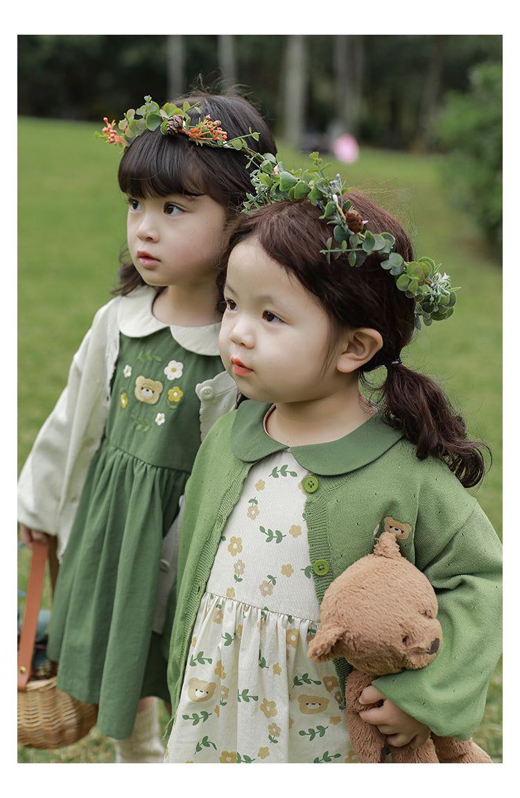 Girls in vibrant green floral dress with collars and floral headbands standing outdoors. 